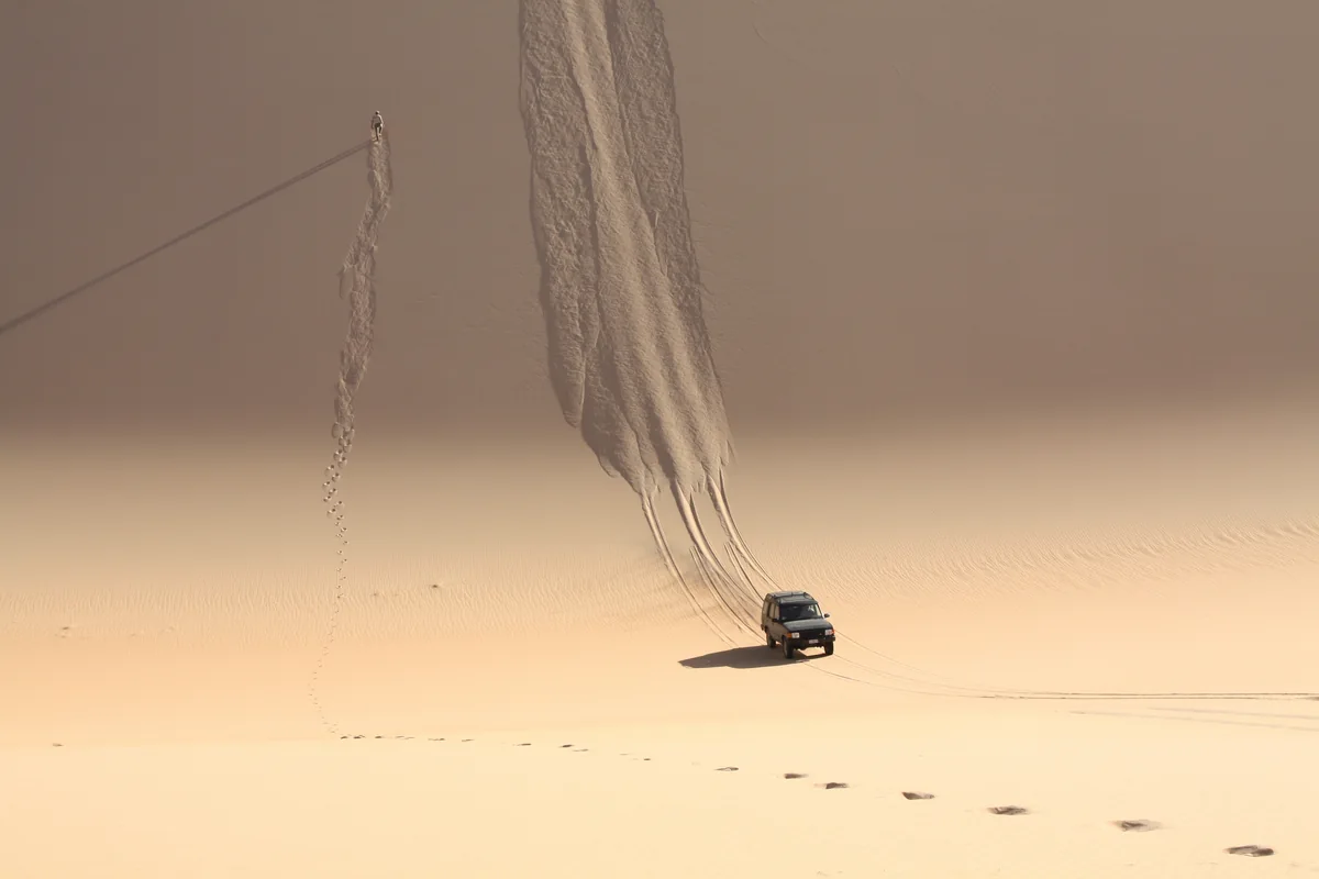 Ein Geländewagen am Fuß einer hohen Sanddüne.