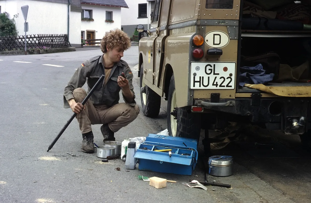 Ein junger Mann arbeitet neben dem offenen Heck eines Land Rover.
