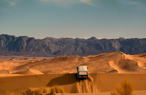 Ein Geländewagen zwischen Sanddünen und Bergen.