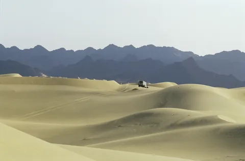 Ein Fahrzeug in einer weiten Dünenlandschaft.