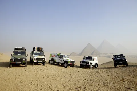 Mehrere Geländewagen in der Wüste vor den Pyramiden.