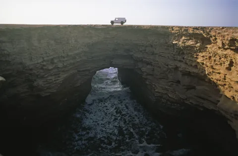 Ein Geländewagen oberhalb eines Felsbogens an der Küste.