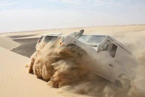 Ein Geländewagen fährt durch den Sand einer Düne.